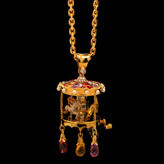 An 18ct yellow gold pendant featuring a miniature carousel with golden horses, diamond mirrors, and sapphire briolettes, suspended from a chain.