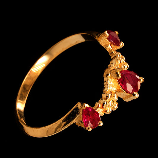 A 9ct rose gold engagement ring featuring a central pear-shaped ruby flanked by two smaller ones, set against a black background.