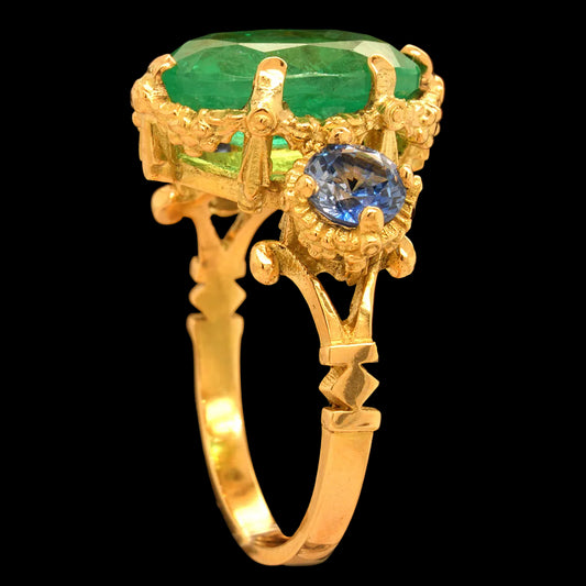 Gold ring with emerald and blue sapphire gemstones on a black background