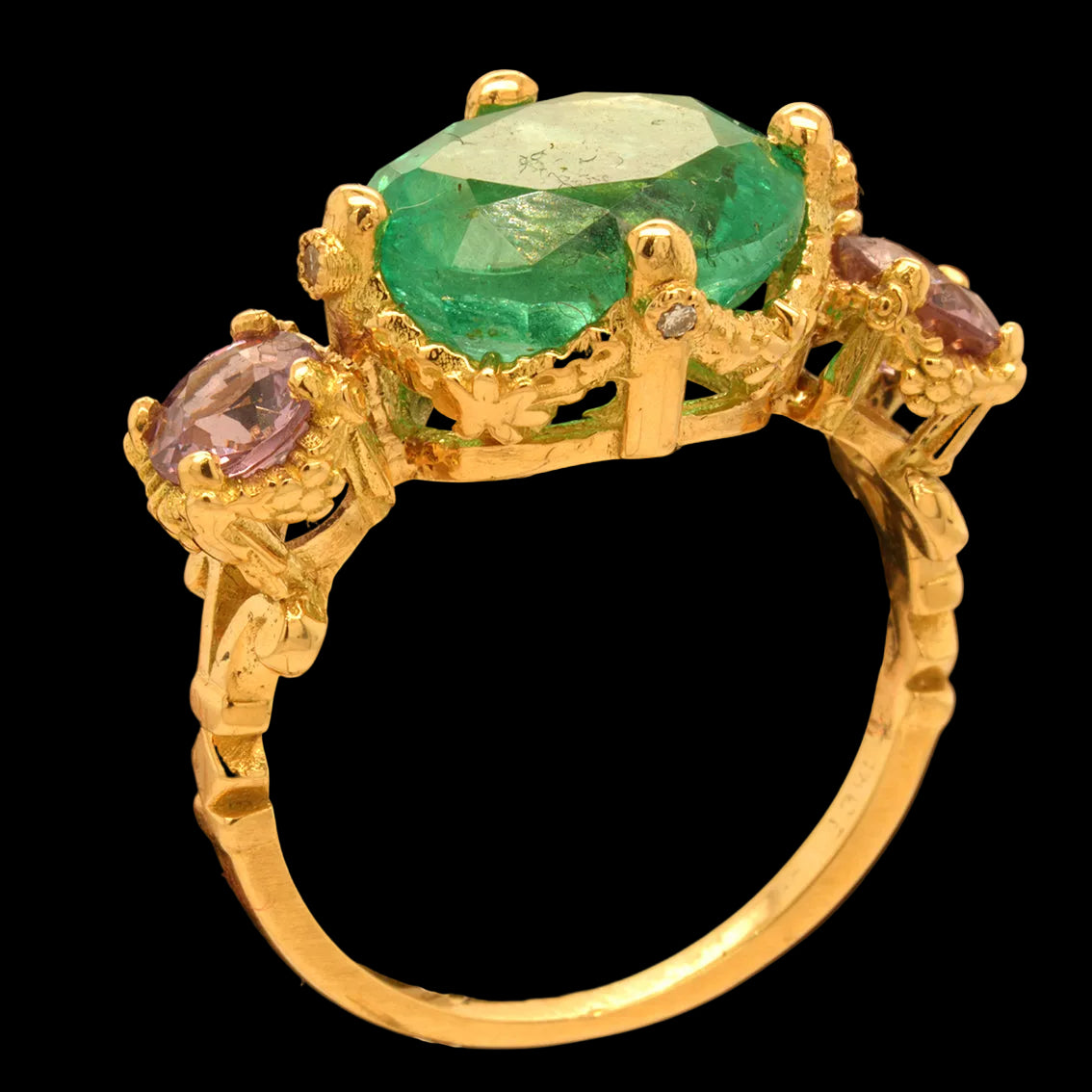 Gold ring with an emerald and purple spinels on a black background
