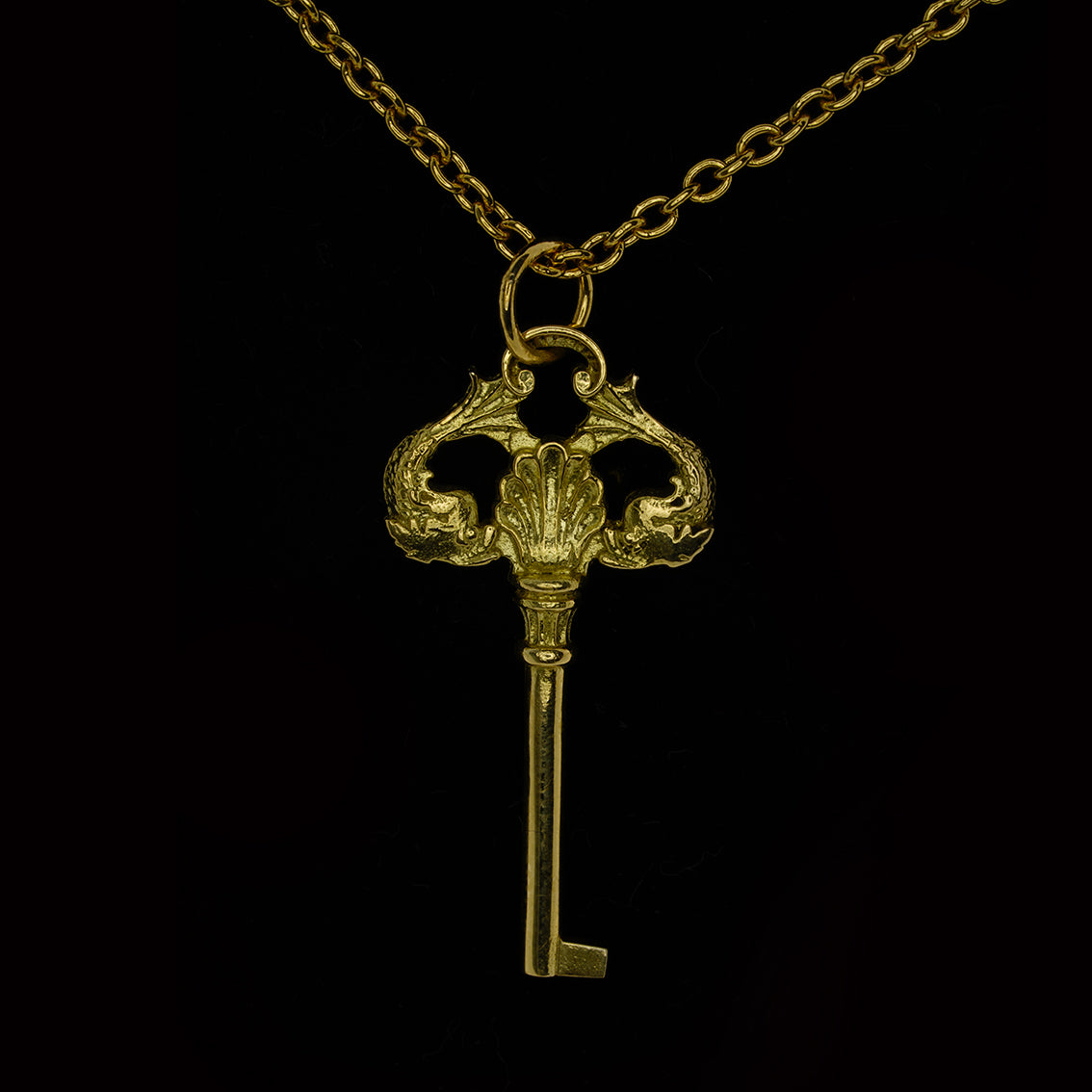 An 9ct yellow gold necklace in the shape of a key with two fish, hanging from a yellow gold curb link chain.