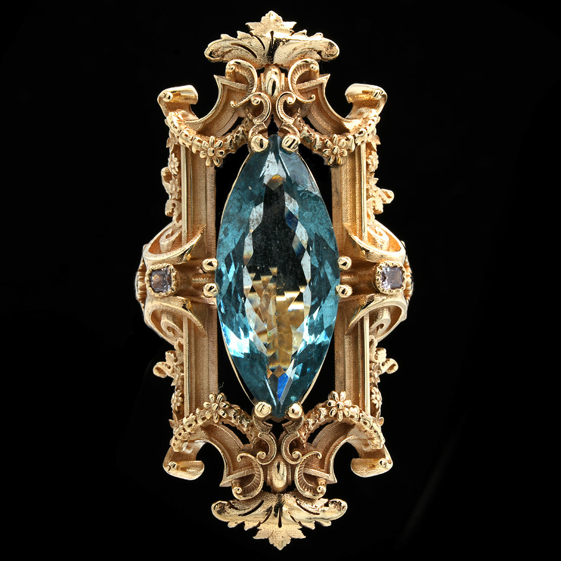 Decorative gold ring with baroque details abd a marquise cut with an aquamarine and pink diamonds a blue gemstone on a black backgroun