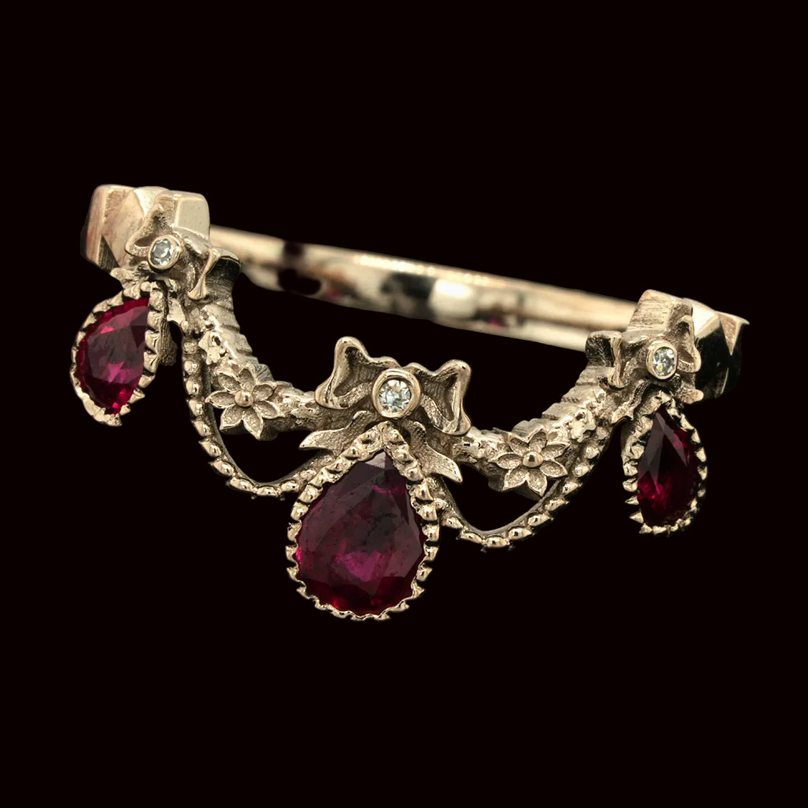 Ornate ring with rubies, bows and diamonds on a dark background