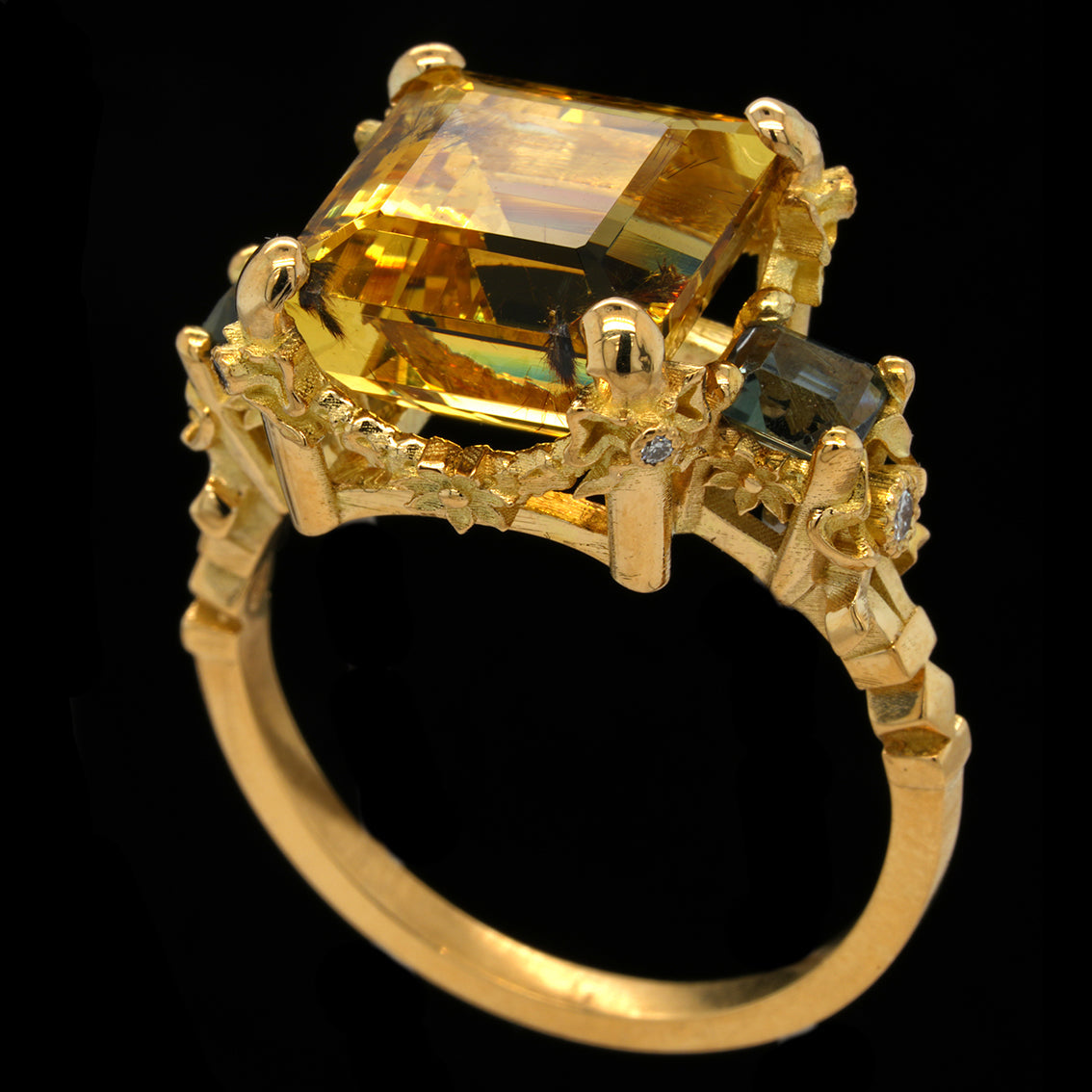 A yellow gold ring featuring a large rectangular emerald-cut yellow gemstone, accented by smaller green and clear stones on the shoulders, set against a solid black background.