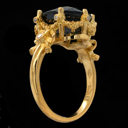 A gold ring featuring a large black oval gemstone in a highly detailed, ornate crown-like setting with small clear accent stones, shown against a solid black background.