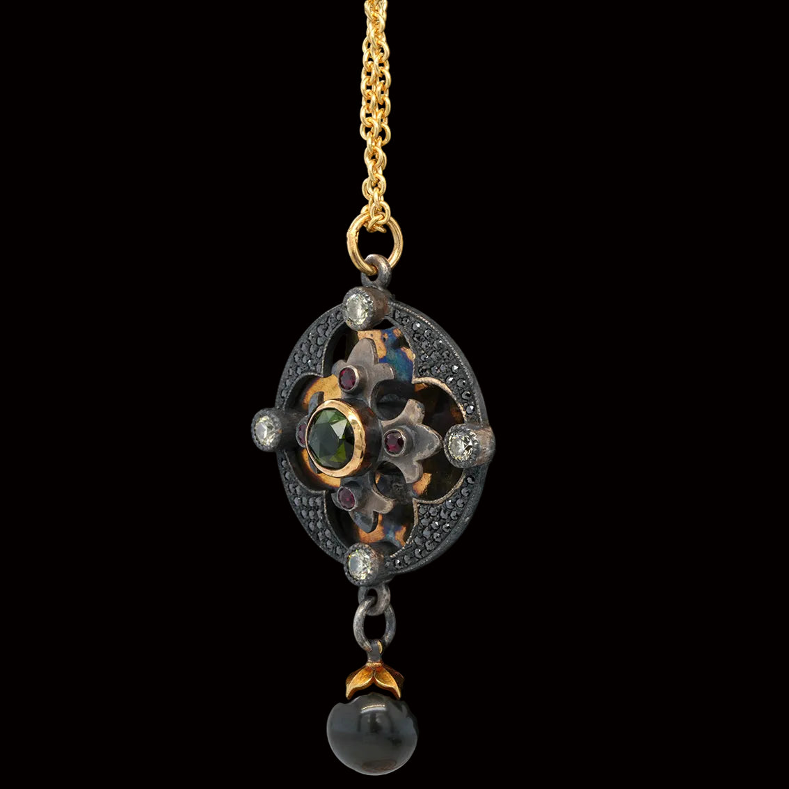 An ornate vintage-style pendant necklace featuring a gold chain, a quatrefoil disk pendant with 18k gold and sterling silver, tourmaline, rubies, diamonds, and a dangling black pearl, displayed against a black background.