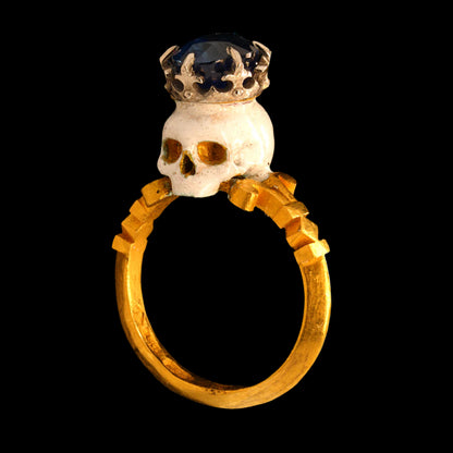 Gold ring with a skull and crown design on a black background