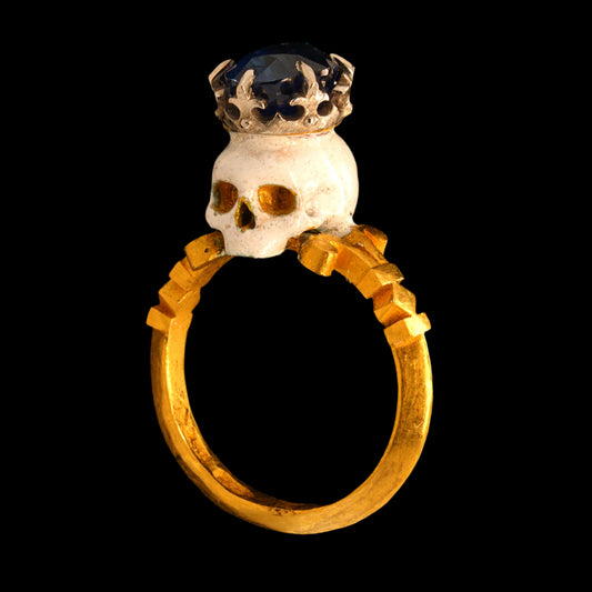 Gold ring with a skull and crown design on a black background
