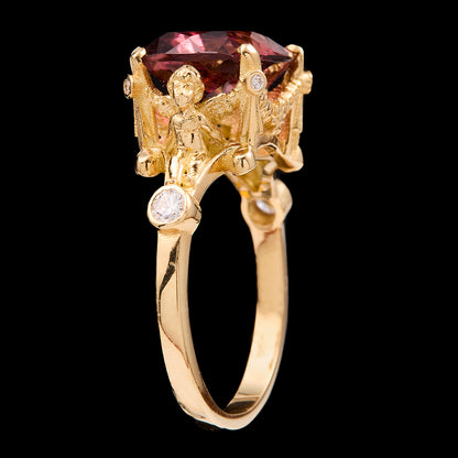 Gold ring with a pink tourmaline, cherubs and smaller diamonds on a black background