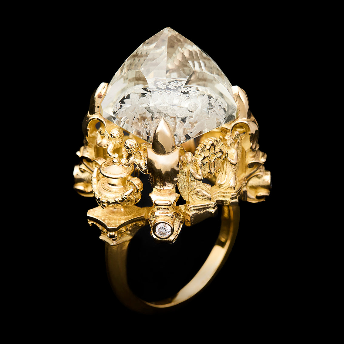 An ornate yellow gold ring featuring a large, reverse intaglio cut citrine in a highly detailed sculpted setting with small accent diamonds, shown against a solid black background.
