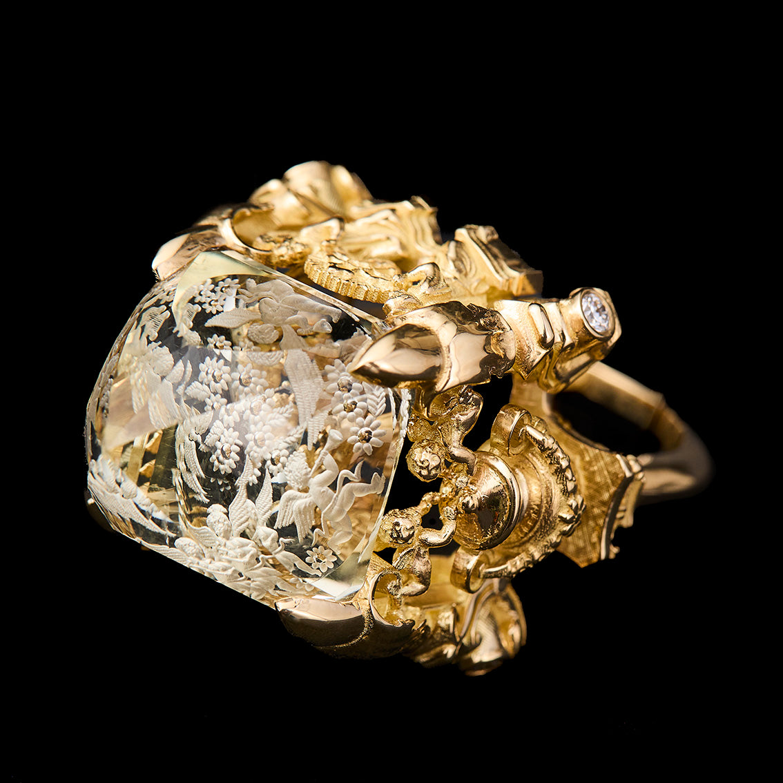 An ornate gold ring featuring a large citrine with intricate floral engravings, set against a solid black background.