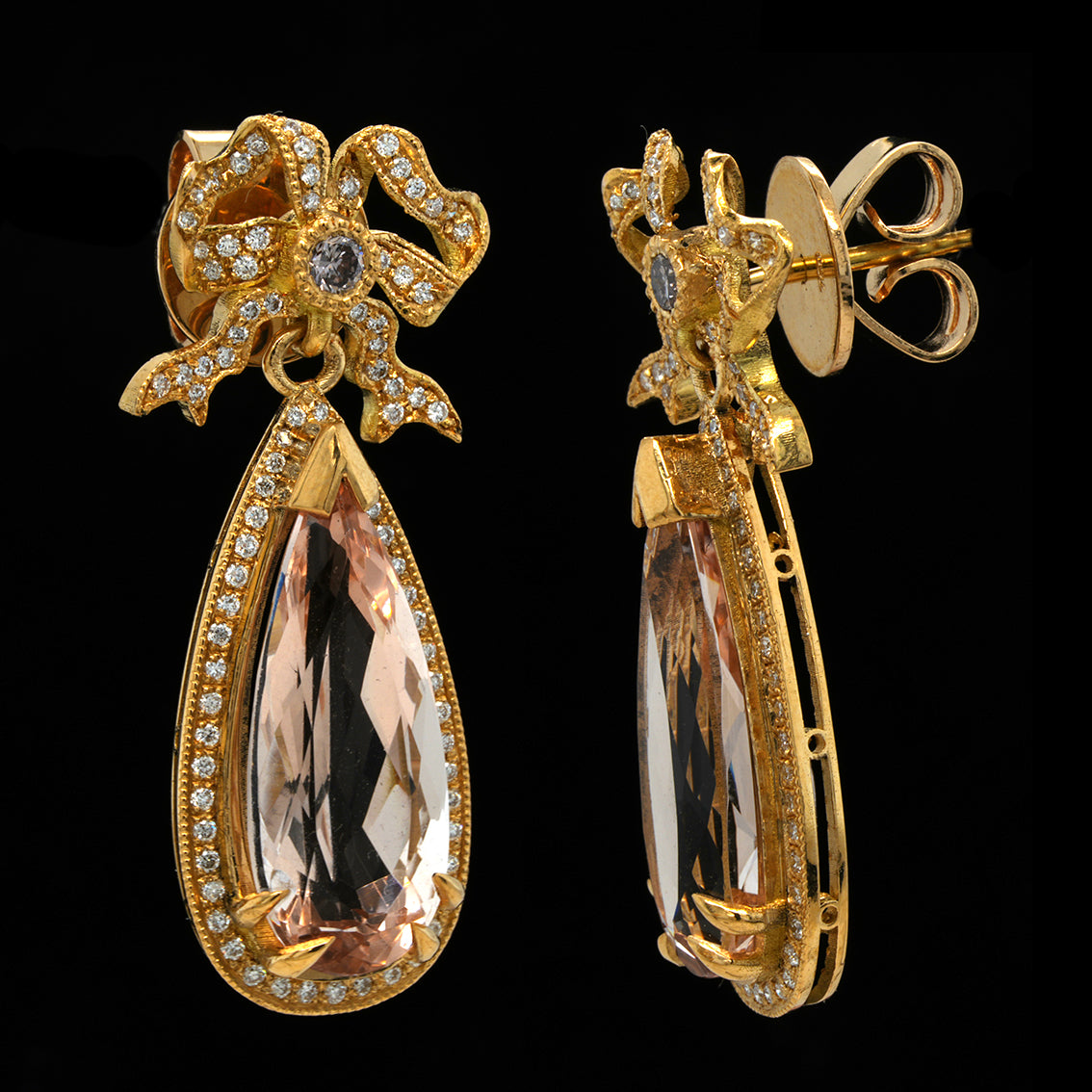 A pair of gold drop earrings featuring large teardrop-shaped peach morganite gemstones surrounded by small diamonds, with decorative bow-like gold tops, shown on a black background.