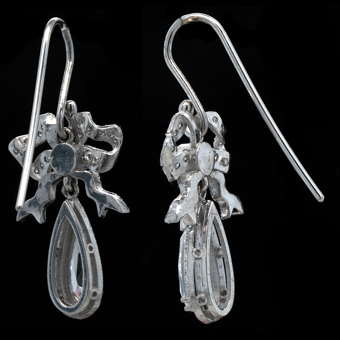 Pair of white gold earrings with bow design on a black background