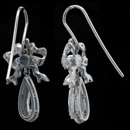 Pair of white gold earrings with bow design on a black background