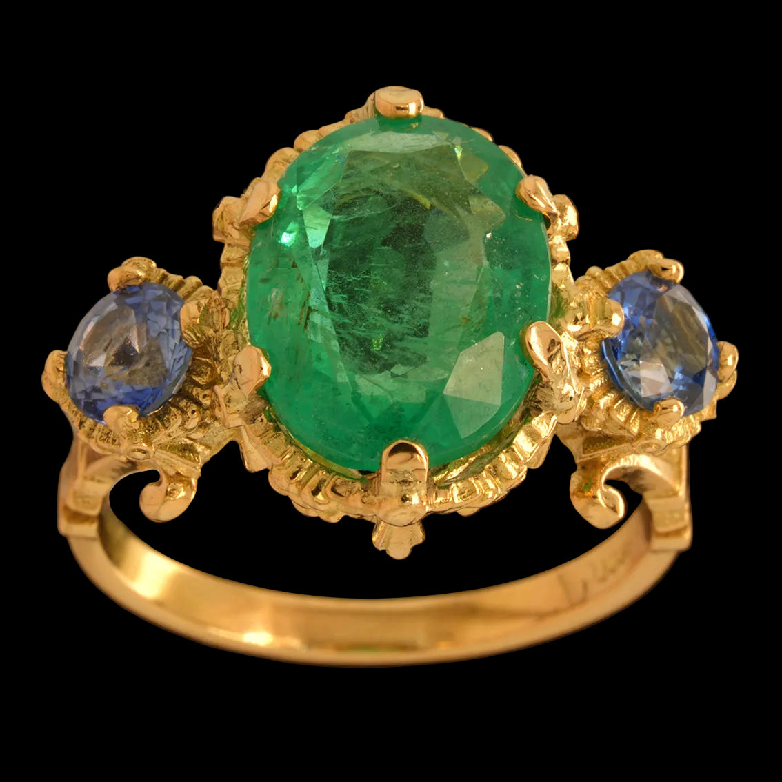 Gold ring with a emerald gemstone and two blue sapphires on a black background
