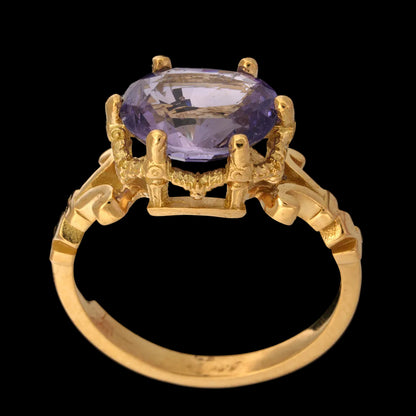 A yellow gold ring featuring an oval-cut light purple sapphire gemstone in a detailed claw setting, shown against a solid black background.