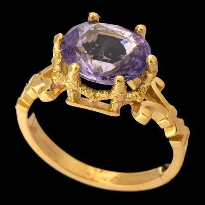 Gold ring with a lilac sapphire gemstone on a black background