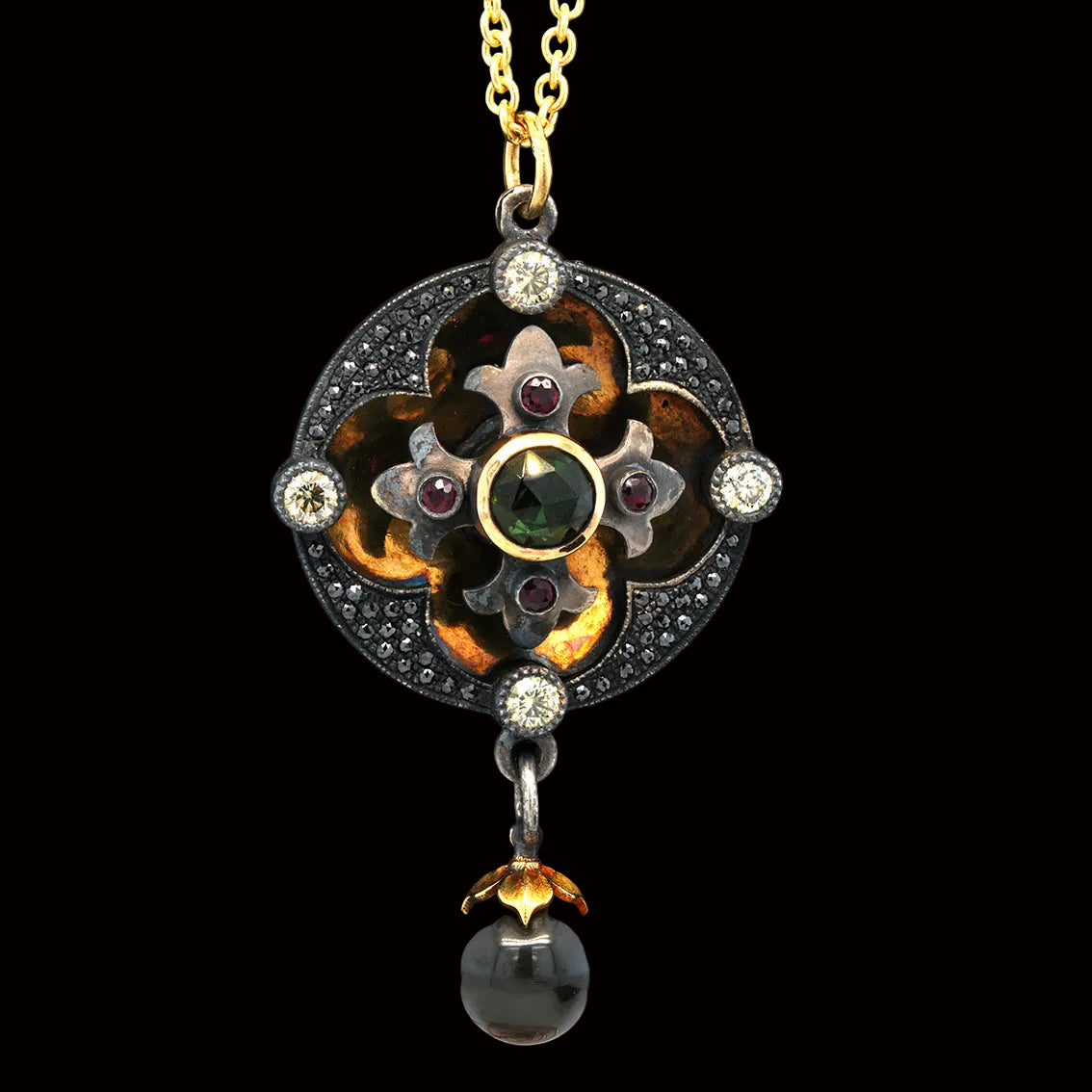 An ornate vintage-style pendant necklace displayed on a black velvet jewelry bust. The pendant features a gold-tone chain, a central floral motif with amber-brown enamel, silver-tone metal, clear stones, and small dark red gemstones, with a dangling oval pearl at the bottom.