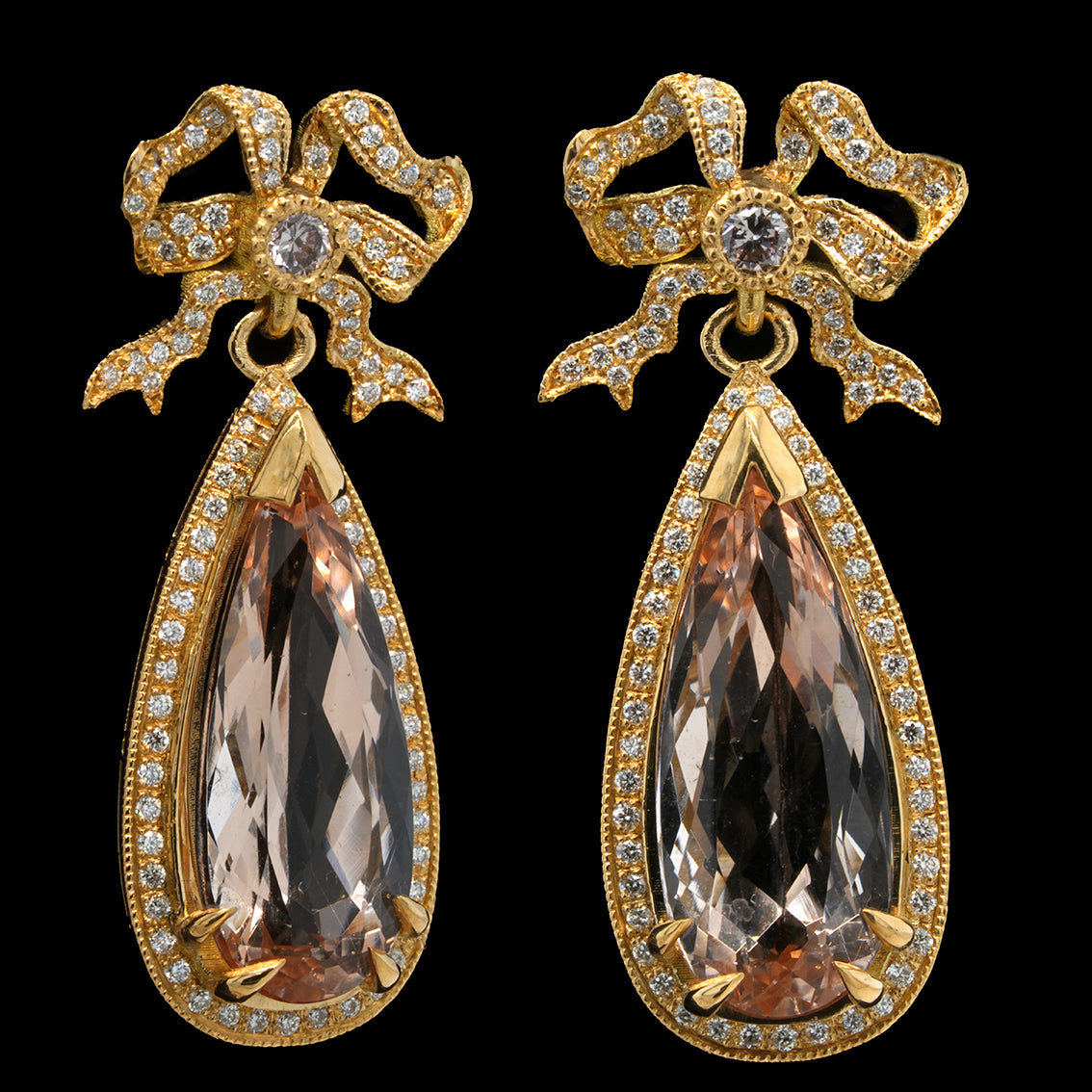 A pair of gold dangle earrings with bow-shaped tops set with diamonds and large pearcut morganites, shown on a solid black background.