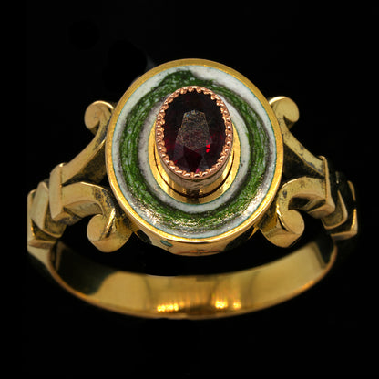 A vintage-style gold ring with a circular face featuring a green ouroborus on a white enamel background, and a central faceted ruby, shown against a solid black background.