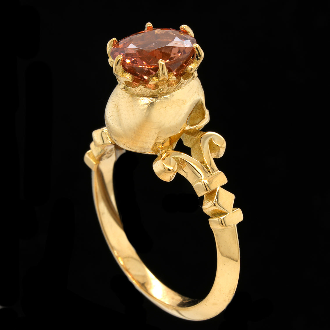A gold ring featuring an oval tourmaline gemstone in a decorative crown-like setting, shown against a solid black background.