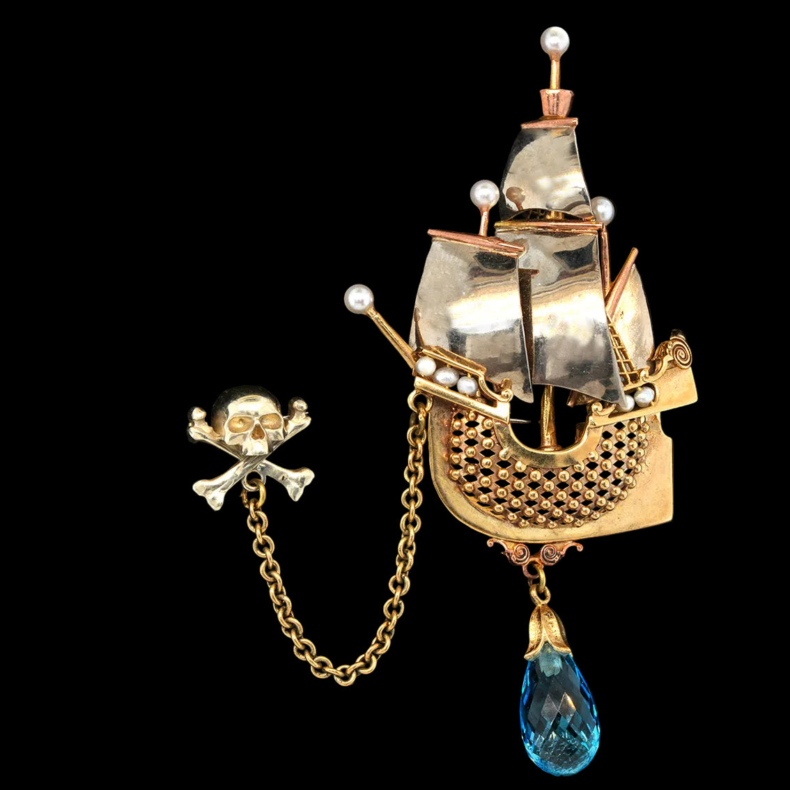 A pirate ship brooch and matching skull-and-crossbones pin on a black background. The ship brooch is gold and silver-tone with white pearl-like accents and a dangling blue teardrop crystal.