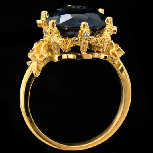 A yellow gold ring featuring a large, faceted teal sapphire in a detailed crown-like setting with small accent diamonds, shown against a solid black background.