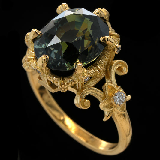 A yellow gold ring featuring a large oval teal sapphire in a detailed claw setting, accented by small diamonds on the band, set against a solid black background.