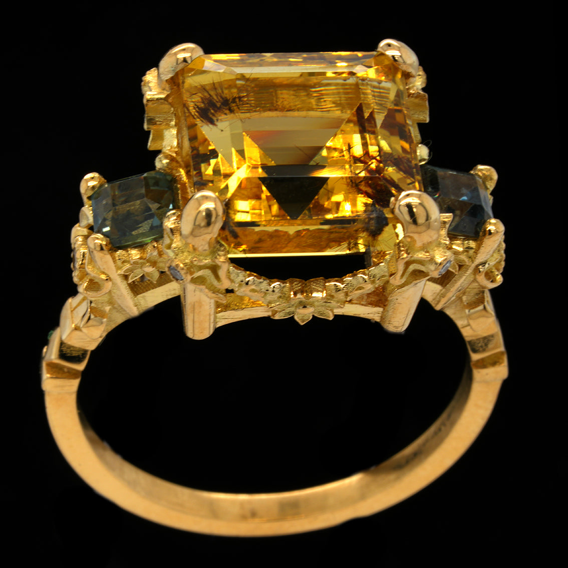 A yellow gold ring featuring a large  yellow aquamarine or heliodor center stone with two smallerteal sapphires on either side, set against a solid black background.