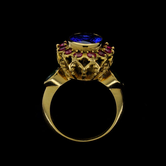 A vibrant yellow gold ring featuring an oval tanzanite stone with a halo of rubies around it and two pear-shaped garnets on the sides, set in a traditional basket setting.