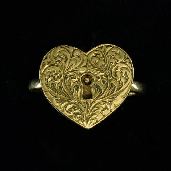 A heart-shaped gold ring with intricate scrollwork and a lockable chamber, displayed against a black background.