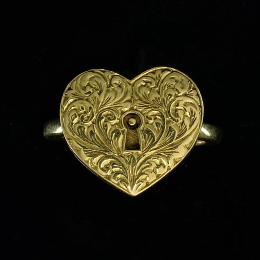 A heart-shaped gold ring with intricate scrollwork and a lockable chamber, displayed against a black background.
