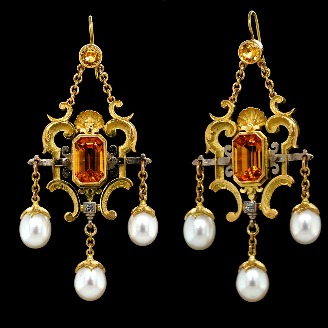 A pair of 18kt yellow and white gold earrings with a central emerald cut sapphire, surrounded by a round yellow sapphire, a princess cut diamond, and cascading white pearls on a golden chain.