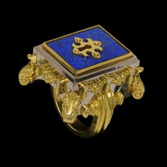 An 18ct yellow gold ring with a lapis lazuli set into a lockable compartment, adorned with rose cut white diamonds, and a fleur de lis design on the key.